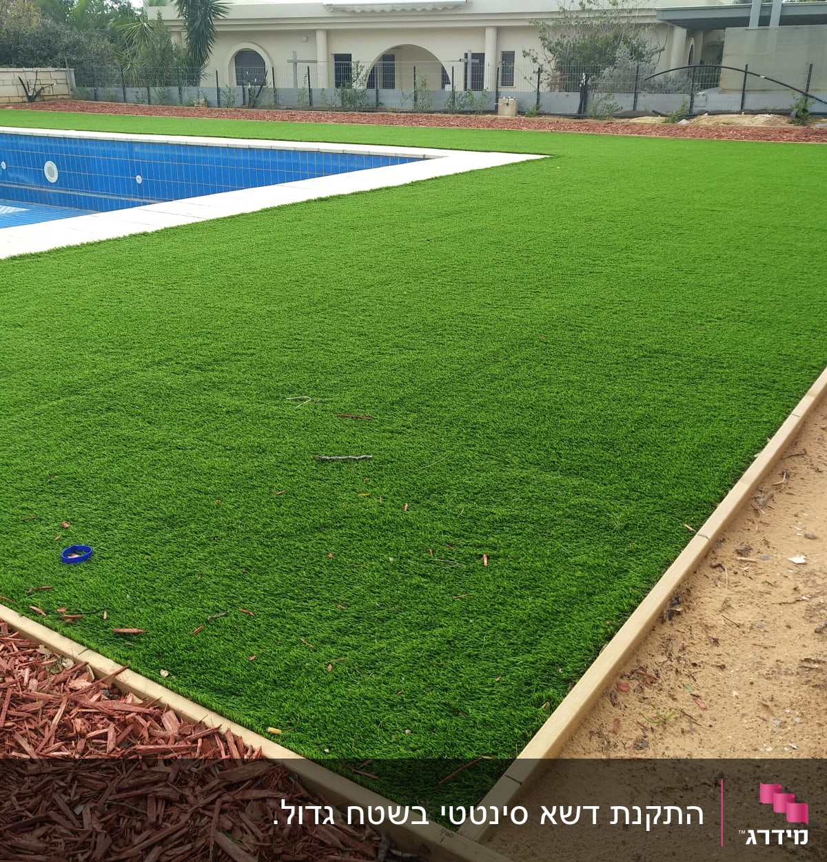 דשא סינתטי ליד בריכה עם שבבי עץ